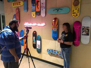 A man and woman standing in front of a wall of skateboards advertising their GoDaddy website for WebCami.