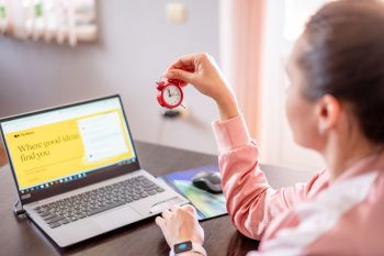 Woman holding a clock in front of a laptop