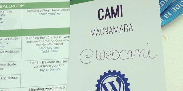 A WordCamp Seattle 2014 attendee badge for Cami MacNamara with the Twitter handle @webcami, placed next to a stripe of lanyard and an event schedule.