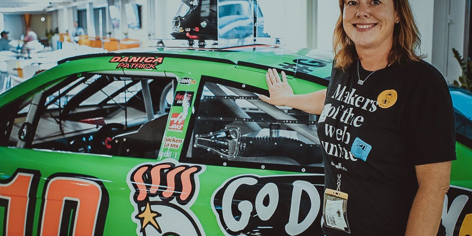 A woman standing next to a NASCAR car featuring the GoDaddy logo.