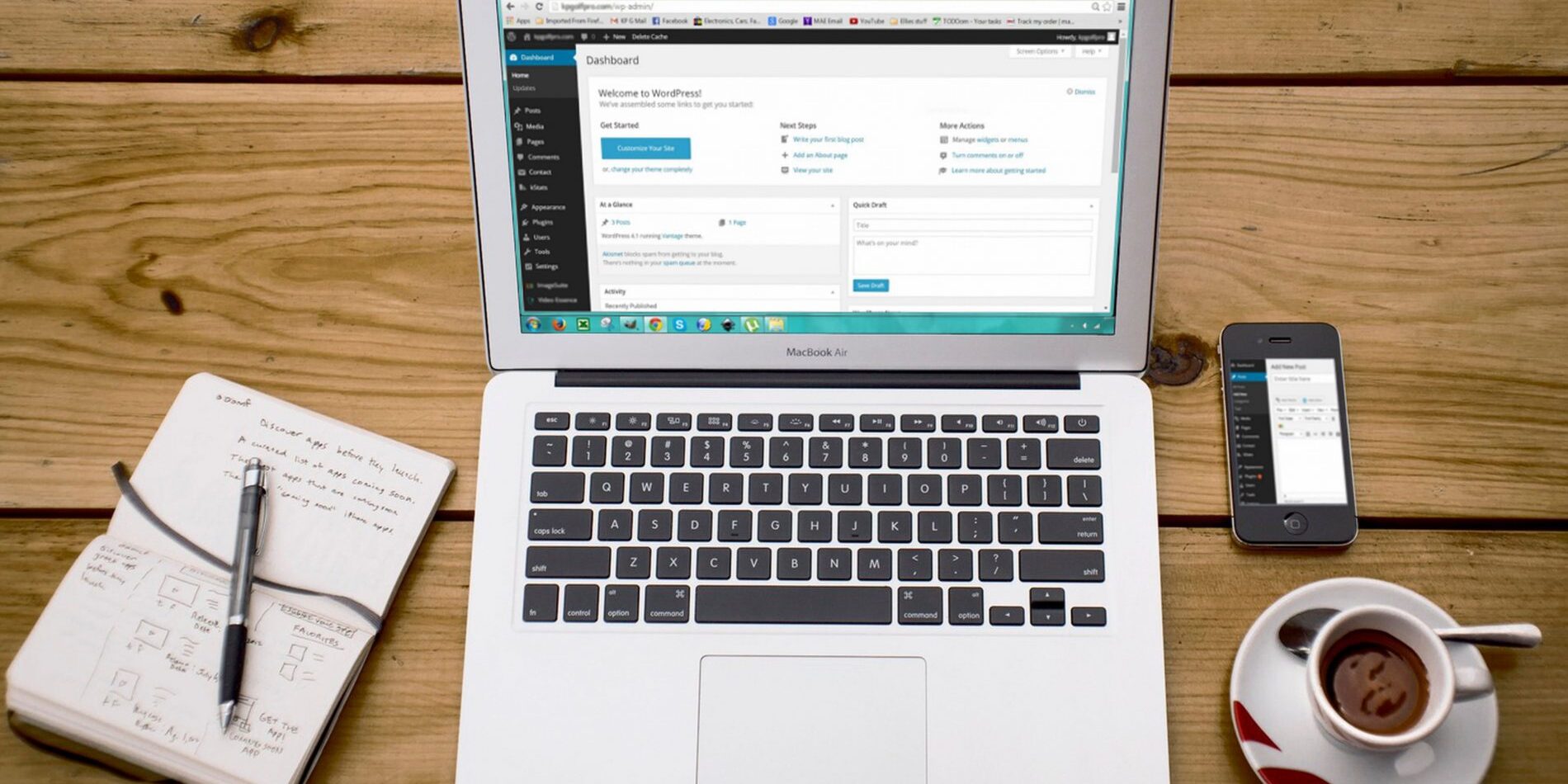 A Classic Editor laptop is sitting on a wooden table next to a phone and a cup of coffee.