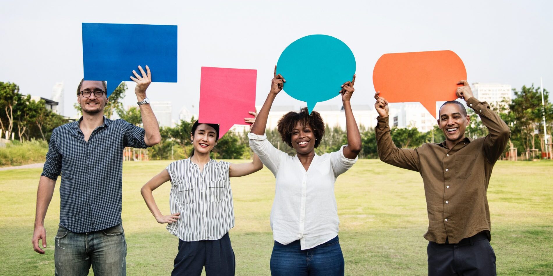 A group of people holding up colorful speech bubbles in a park, engaging in lively conversations.