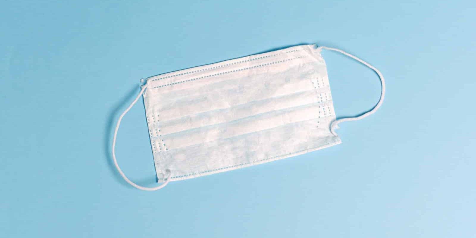 A white surgical mask worn during video conferencing with a blue background.