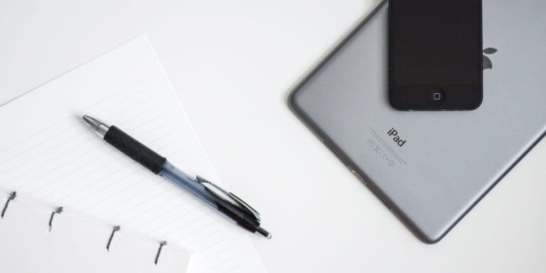An iPad and a pen placed next to a notebook for systems organization and year in review.