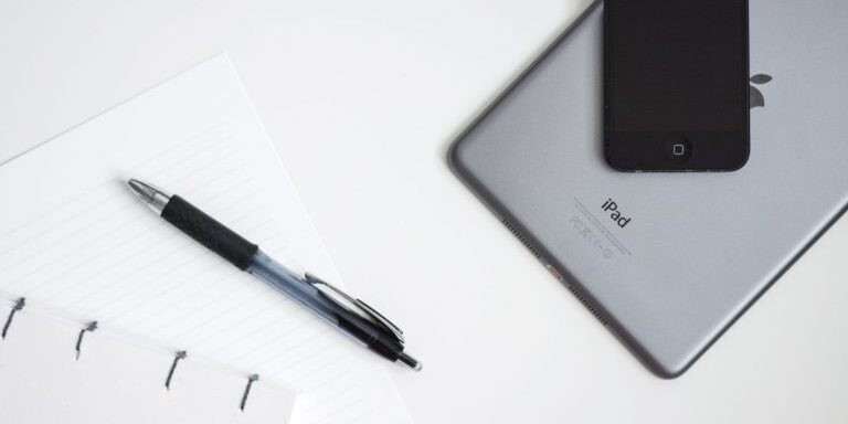 An iPad and a pen placed next to a notebook for systems organization and year in review.